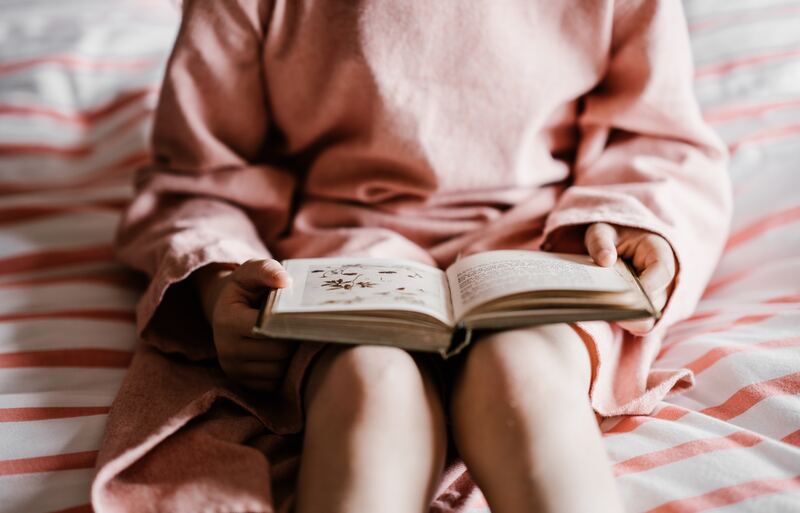 A child sitting on a bed reading a book.
