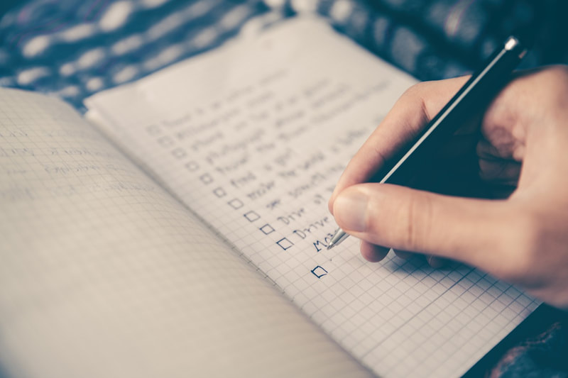Person writing a checklist in a notebook.