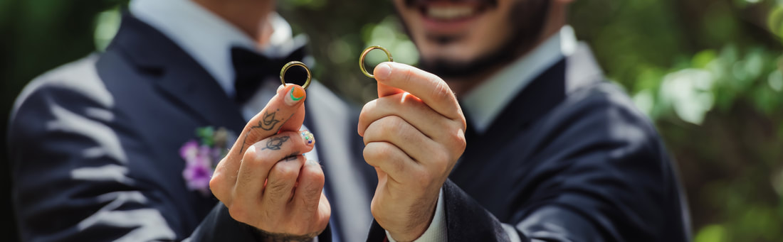 A male couple holding their wedding rings close to the camera.