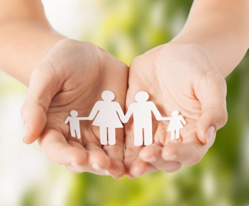 A pair of hands holding paper cutouts of a family holding hands.