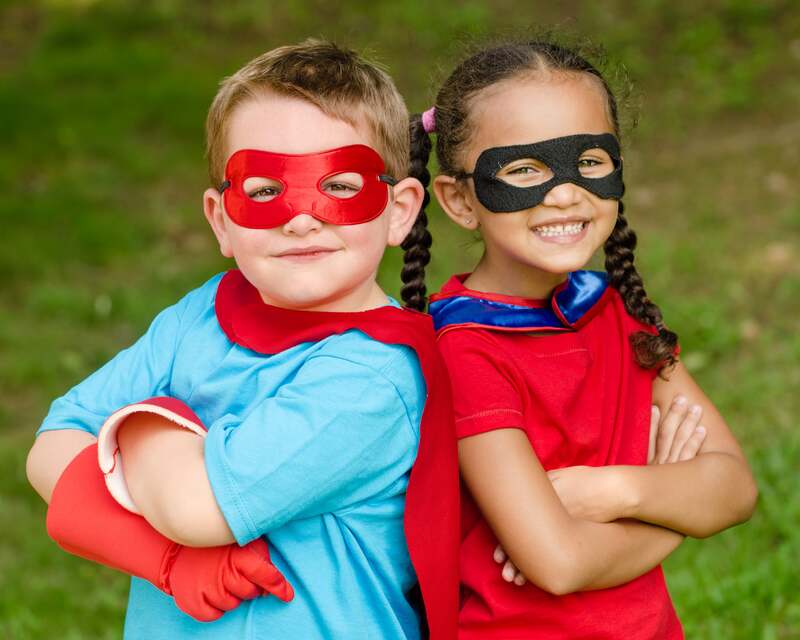 Two young children dressed up as superheroes with their backs to each other and their arms folded.