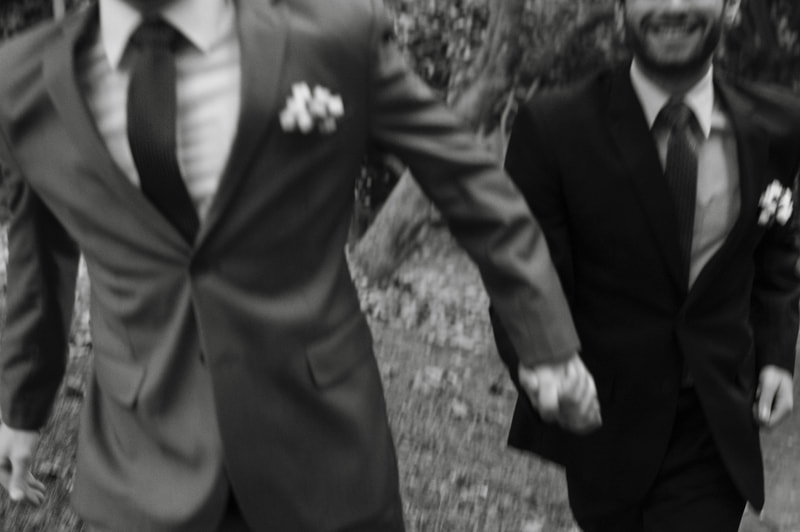 Wedding photo of two grooms holding hands and walking towards camera.